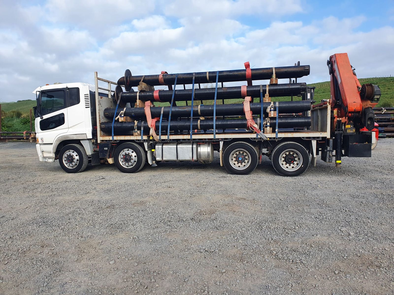 The crane truck side-on with four tiers of black steel pipe on timber dunnage, ratchet-strapped